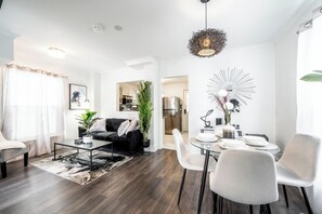 A modern living room with a sofa, coffee table, and dining area. - Cozy Home w/ parking, Walk to Clifton Hills, 10mins to The Falls, Fire Pit &more (Niagara Falls)
