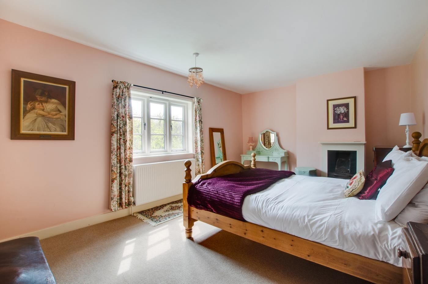A bedroom with a wooden bed, a dresser, a mirror, a fireplace, and a window with curtains.