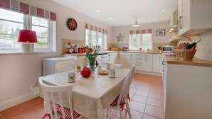 Une cuisine moderne avec des meubles blancs, une table à manger avec des chaises, une lampe rouge et une horloge au mur.