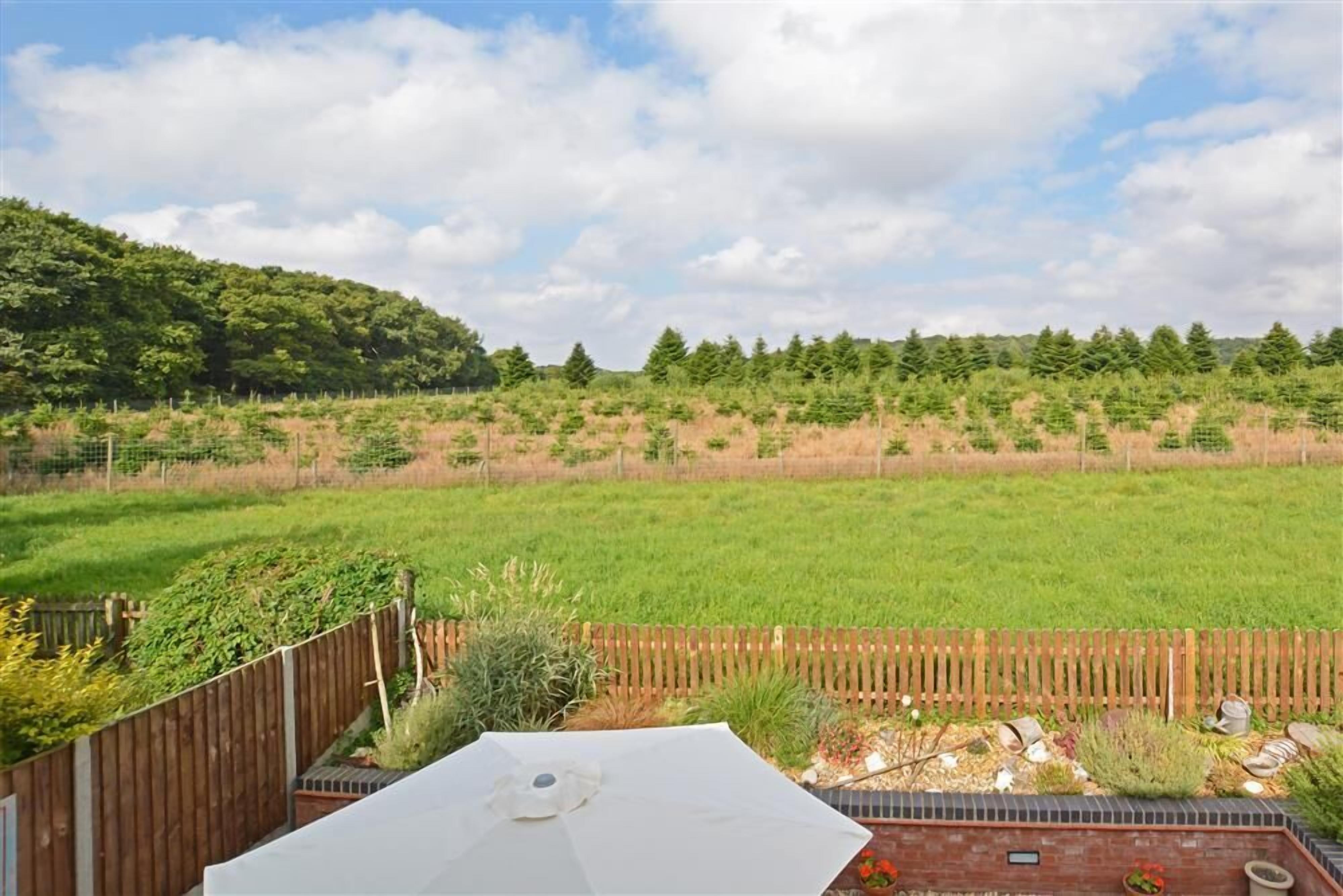 A backyard with a wooden fence, a brick patio, and a grassy field.