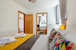 A bedroom with a bed, a dresser, a window with curtains, and a door leading to another room.
