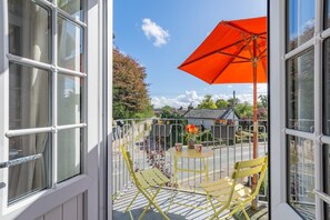 A balcony with yellow chairs, a table, and an orange umbrella.