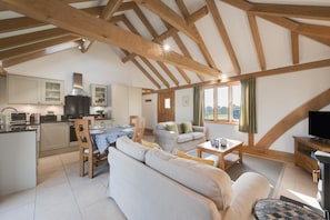 A spacious loft with exposed wooden beams, a kitchen with modern appliances, a dining area, and a living room with a sofa and a television.
