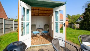 Een klein, afgesloten terras met een houten plafond, twee stoelen en een tafel.