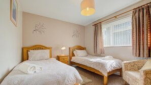 Een slaapkamer met twee houten bedden, een nachtkastje, een stoel en een raam met gordijnen.