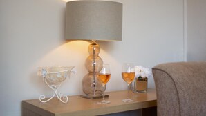 Een nachtkastje met een lamp, twee wijnglazen en een vaas met bloemen.