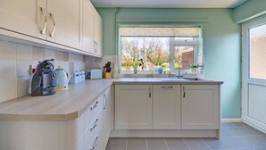 A modern kitchen with white cabinets, a light-colored countertop, and a window providing a view of the outdoors. - 2 Bed in Wells-next-the-Sea (oc-1655) (Wells-next-the-Sea)