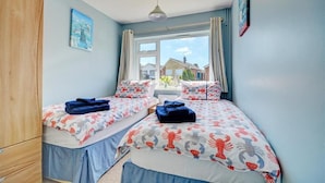 A bedroom with two beds, a wooden wardrobe, a window with curtains, and a painting on the wall. - 2 Bed in Wells-next-the-Sea (oc-1655) (Wells-next-the-Sea)