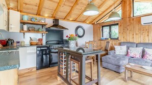 A cozy cabin interior with a kitchen, dining area, and living room, featuring wooden walls and floors, a stove, and a clock. - 1 Bed in Whitbourne (oc-s32935) (Whitbourne)