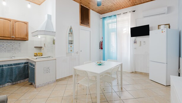 A kitchen with white cabinets, a tiled backsplash, a white dining table with chairs, a ceiling fan, and a white refrigerator. - Perla Marina Ground Floor Apartment with Wi-Fi and Air Conditioning (Trappeto)