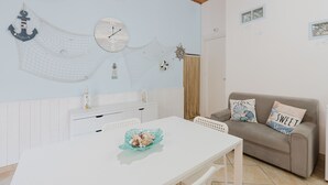 A room with a white table, a beige sofa, nautical wall decorations, and a clock. - Perla Marina Ground Floor Apartment with Wi-Fi and Air Conditioning (Trappeto)