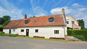 Ein zweistöckiges Steinhaus mit einem Ziegeldach, ein kleiner Garten mit roten Blumen und einem strahlend blauen Himmel.