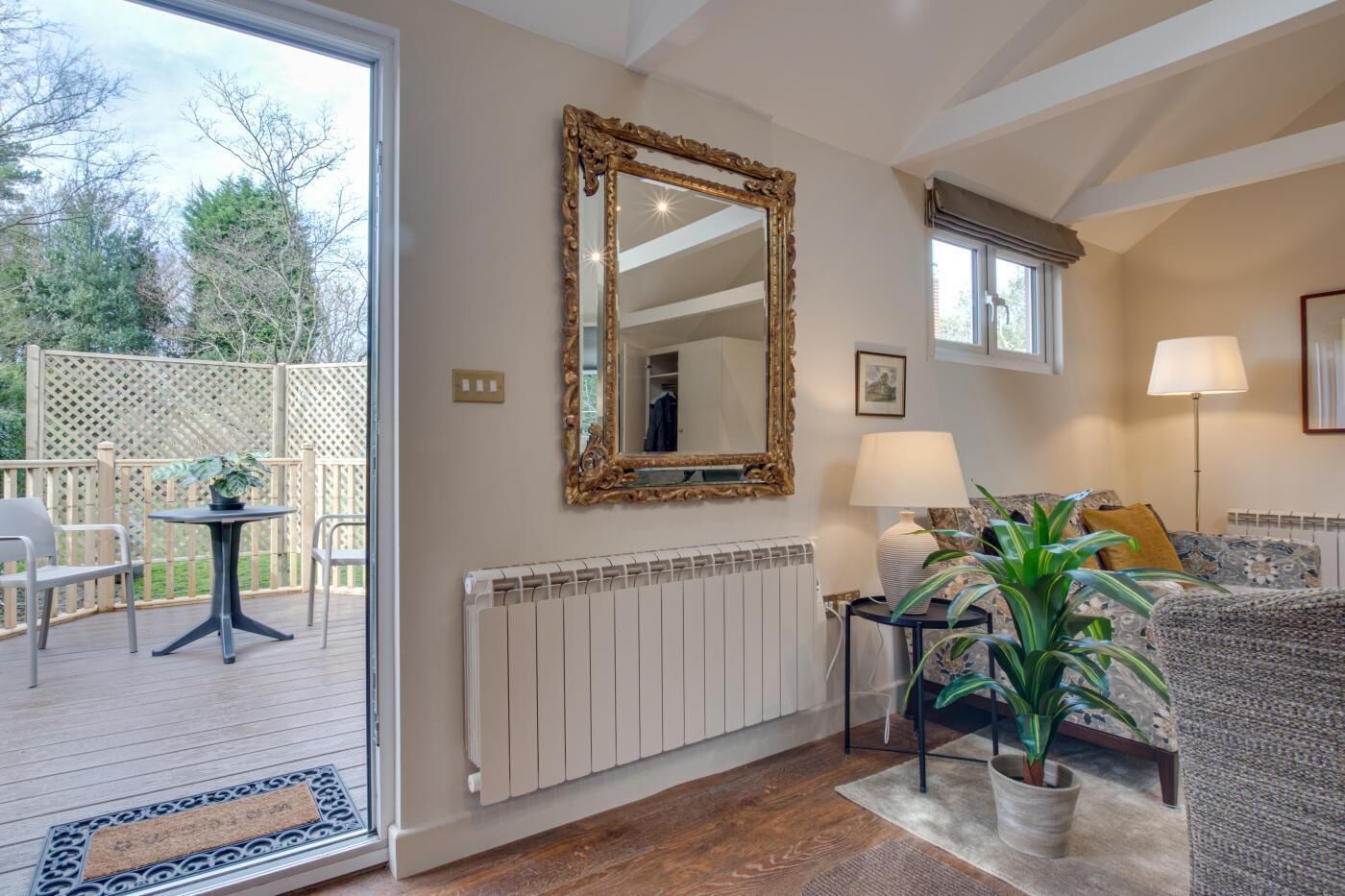 Een kamer met een grote spiegel, een radiator, een bank, een tafel met stoelen en een potplant.