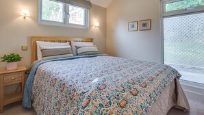 Un dormitorio con cama, mesitas de noche, una ventana con persianas y una lámpara de pared.