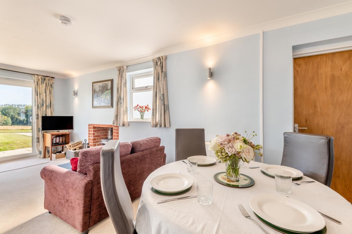 A dining area with a table set for four, a fireplace, a television, and a view of the outdoors.