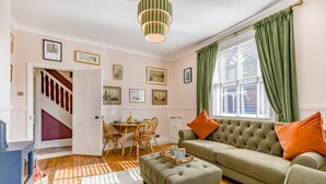 A cozy living room with a sofa, ottoman, and dining table. A staircase leads to another room. - 2 Bed in Cromer (oc-s32971) (Cromer)