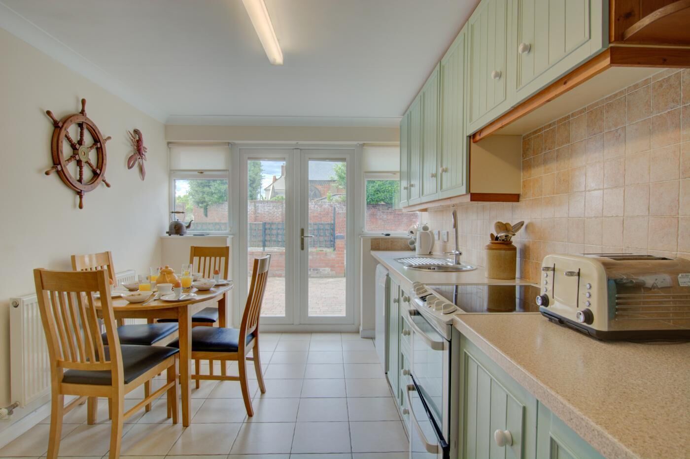 Une cuisine avec un coin repas, comprenant une table et des chaises en bois, une cuisinière, un grille-pain et une vue à travers la porte vitrée.