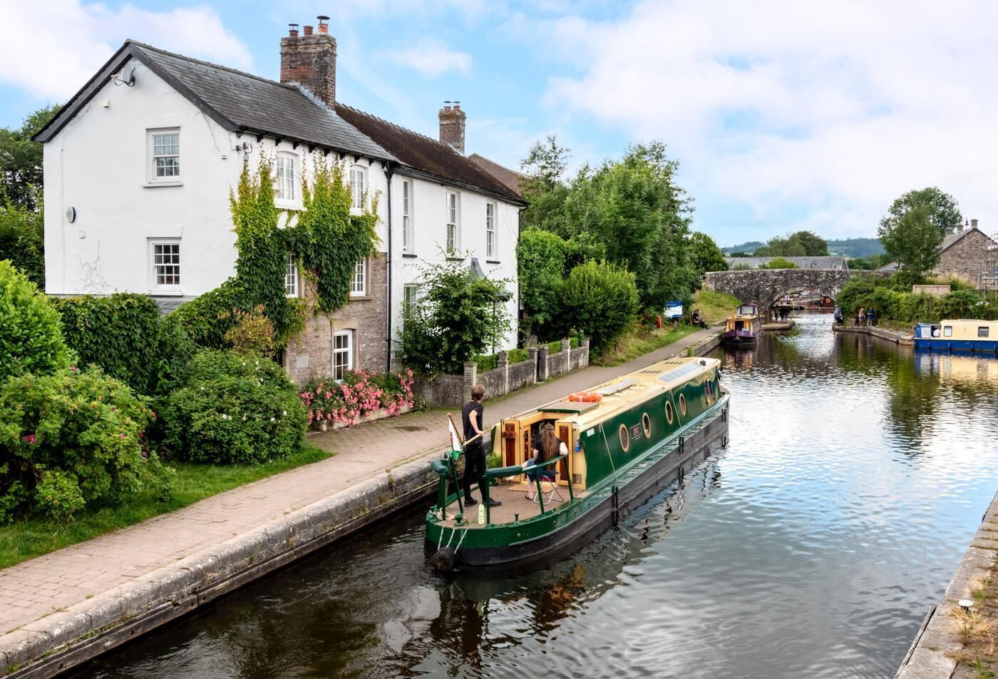 A narrow canal with a house on the left and a green boat moored alongside.