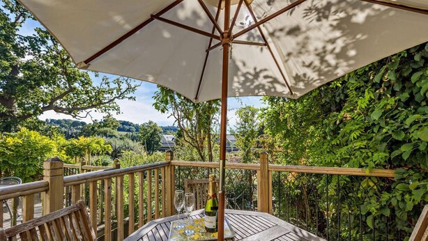 Un terrazzo in legno con un tavolo apparecchiato per un pasto, circondato da rigogliosa vegetazione e vista sulla campagna.