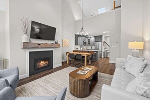 A modern living room with a fireplace, a television, and a dining area. - Luxury Winterplace Condo Steps from the Lifts (Ludlow)
