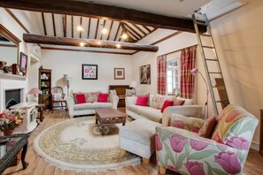 Ein gemütliches Wohnzimmer mit Kamin, Sofas mit floralem Muster, einem Holztisch und einer Wandleiter.