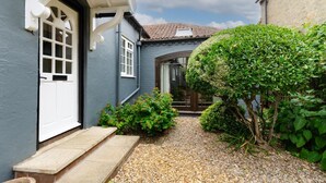 Un étroit sentier mène à une maison avec une porte blanche et un petit porche.