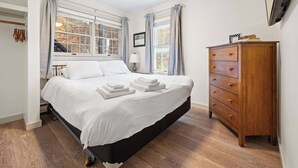 A bedroom with a bed, a wooden dresser, and a window with curtains. - Bright 2BR Escape 2 Min to Okemo, Walk to Downtown (Ludlow)