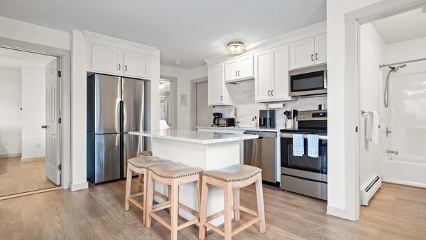 A modern kitchen with white cabinetry, stainless steel appliances, and a central island with stools. - Bright 2BR Escape 2 Min to Okemo, Walk to Downtown (Ludlow)
