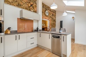 A modern kitchen with white cabinetry, a dishwasher, and a stone accent wall. - 2 Bed in Grimston (oc-1622) (Grimston)