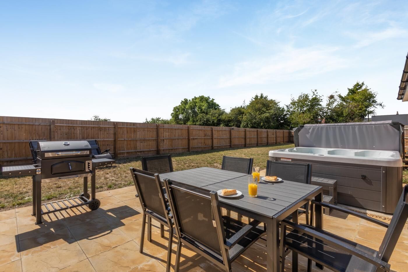 Una terrazza esterna con barbecue, vasca idromassaggio e tavolo da pranzo con sedie.
