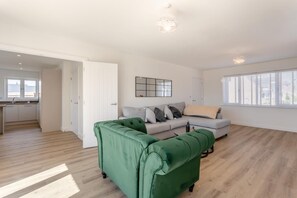 Ein modernes Wohnzimmer mit einem grünen Sofa, einem grauen Sofa und einem Couchtisch. Es gibt eine Küchenzeile mit einem Fenster und einer Tür, die in einen anderen Raum führt.