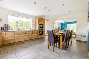 Une cuisine moderne avec des meubles en bois, un coin repas comprenant une table et des chaises, et une vue sur l’extérieur.