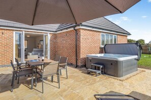 A patio with a table, chairs, and a hot tub under a large umbrella.