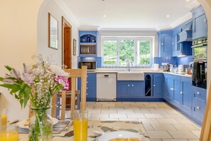 A modern kitchen with blue cabinets, a dishwasher, and a window providing natural light. - 4 Bed in Sedgeford (oc-918) (Sedgeford)