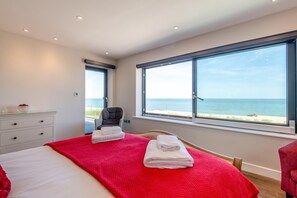 A bedroom with a bed, a chair, a dresser, and a large window with a view of the beach. - 5 Bed in Walmer (oc-do022) (Kingsdown)