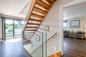 A modern interior with a glass staircase, wooden floor, and a view of greenery outside. - 5 Bed in Walmer (oc-do022) (Kingsdown)