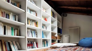 A room with wooden flooring, white bookshelves filled with books, a blue bean bag, and a patterned rug. - House in the center Bergamo (Bergamo)