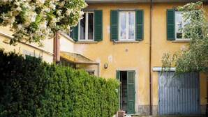 A yellow building with green shutters, a metal gate, and a hedge. - House in the center Bergamo (Bergamo)