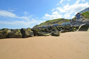 A beach with large rocks, a staircase leading to a building, and a train in the background. - 2 Bed in Sheringham (oc-1540) (Sheringham)