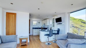 A modern kitchen with a central island, bar stools, and a TV mounted above the island. - 2 Bed in Sheringham (oc-1540) (Sheringham)