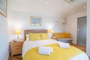 Une chambre d’hôtel avec un lit, deux tables de chevet, une chaise, une porte et un tableau encadré au mur.