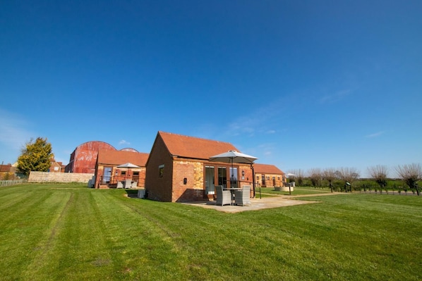 A large building with a brick exterior, a covered patio area with outdoor seating, and a well-maintained lawn.