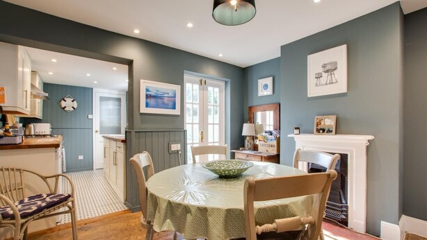 A dining area with a round table, chairs, a bowl, a fireplace, and a kitchen in the background. - 3 Bed in Whitstable (oc-ek768) (Whitstable)