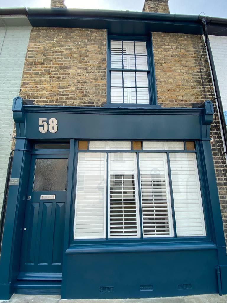 A two-story building with a dark blue facade, a brick upper section, and a large window with white shutters.