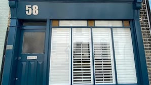 A two-story building with a dark blue facade, a brick upper section, and a large window with white shutters. - 3 Bed in Whitstable (oc-ek768) (Whitstable)