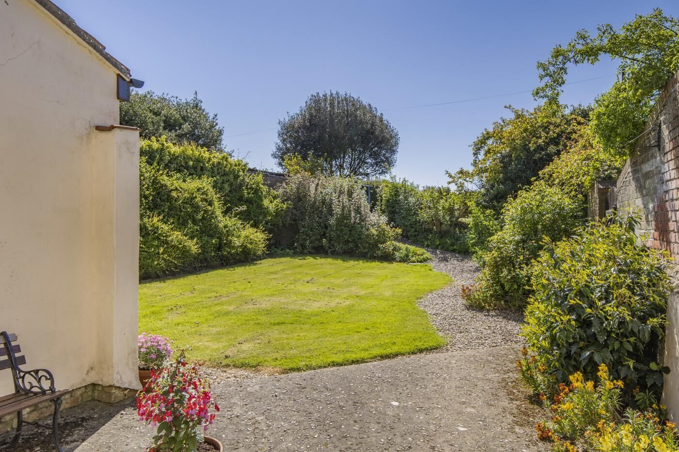 Ein Garten mit Rasenfläche, Kiesweg und unterschiedlichen Pflanzen.