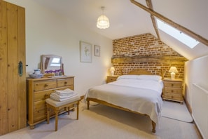Une chambre à coucher avec un lit en bois, une commode, un banc, une table de chevet, une lampe et une lucarne.
