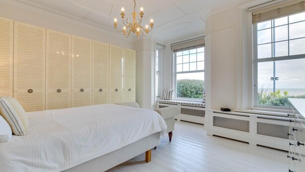 Une chambre dotée d’un grand lit, d’une armoire intégrée, d’un banc près de la fenêtre et offrant une vue sur la verdure environnante.