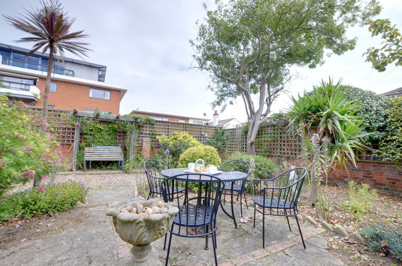 A patio with a round table and chairs, surrounded by plants and a brick wall.