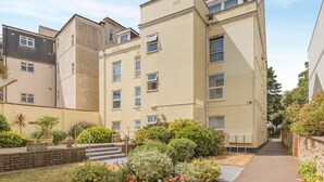 A multi-story residential building with a central staircase, a small garden area with various plants, and a clear sky. - 2 Bed in Sidmouth (oc-t32948) (Sidmouth)
